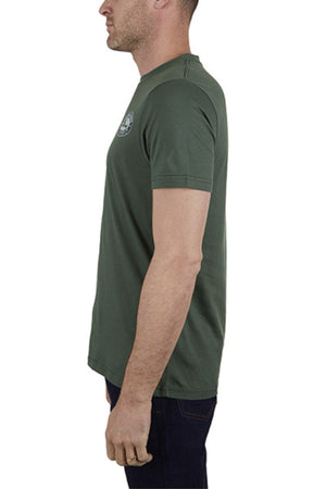 A man stands in profile facing left against a white background, wearing a green 100% cotton Thomas Cook Oval Tee (classic fit) and dark jeans.