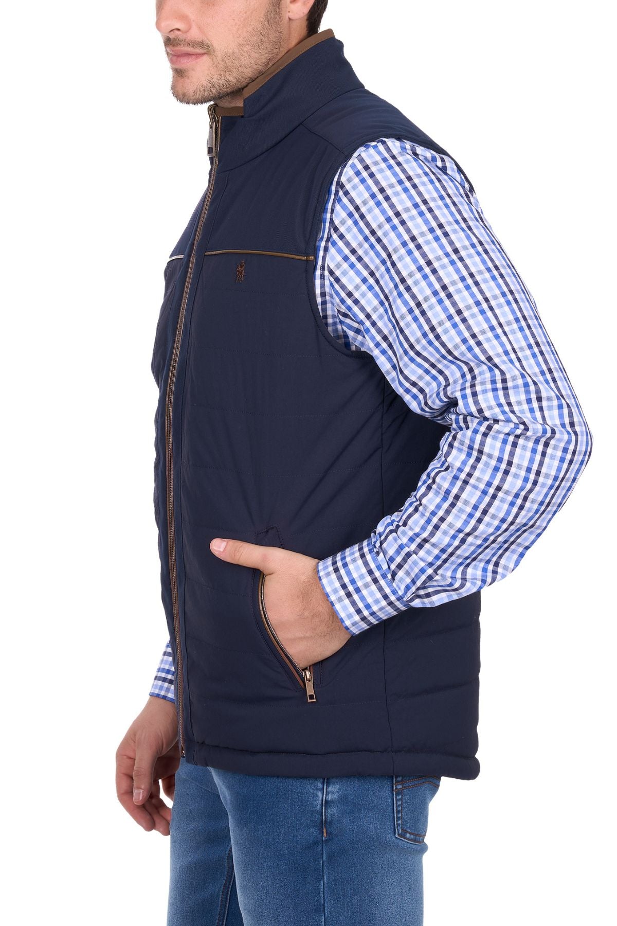A man wears the Thomas Cook Toby Revs Vest, a navy blue quilted vest with zippered pockets, over a blue checkered shirt, standing with one hand in his pocket against a white background.