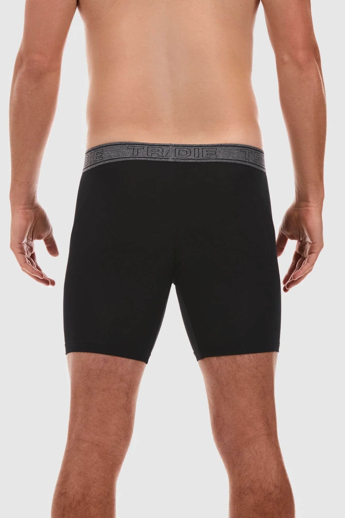 A person stands with their back to the camera, wearing black Tradie Bamboo No Chafe Long Leg Trunks featuring an elastic waistband that has "TRIDE" written on it in a repeated pattern. The person is shirtless, showcasing their bare back and legs against a plain white background. The trunks are made from breathable stretch material for ultimate comfort.