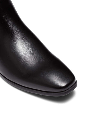 Close-up of the toe of the UNcut Newlands Boot, a sleek black leather shoe with a shiny finish and an almond toe shape, set against a white background.