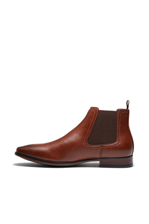 The UNcut Newlands Boot, a versatile Chelsea boot designed with an almond toe shape, is crafted from sleek brown leather. It features elastic side panels and a low heel, all elegantly showcased against a white backdrop.