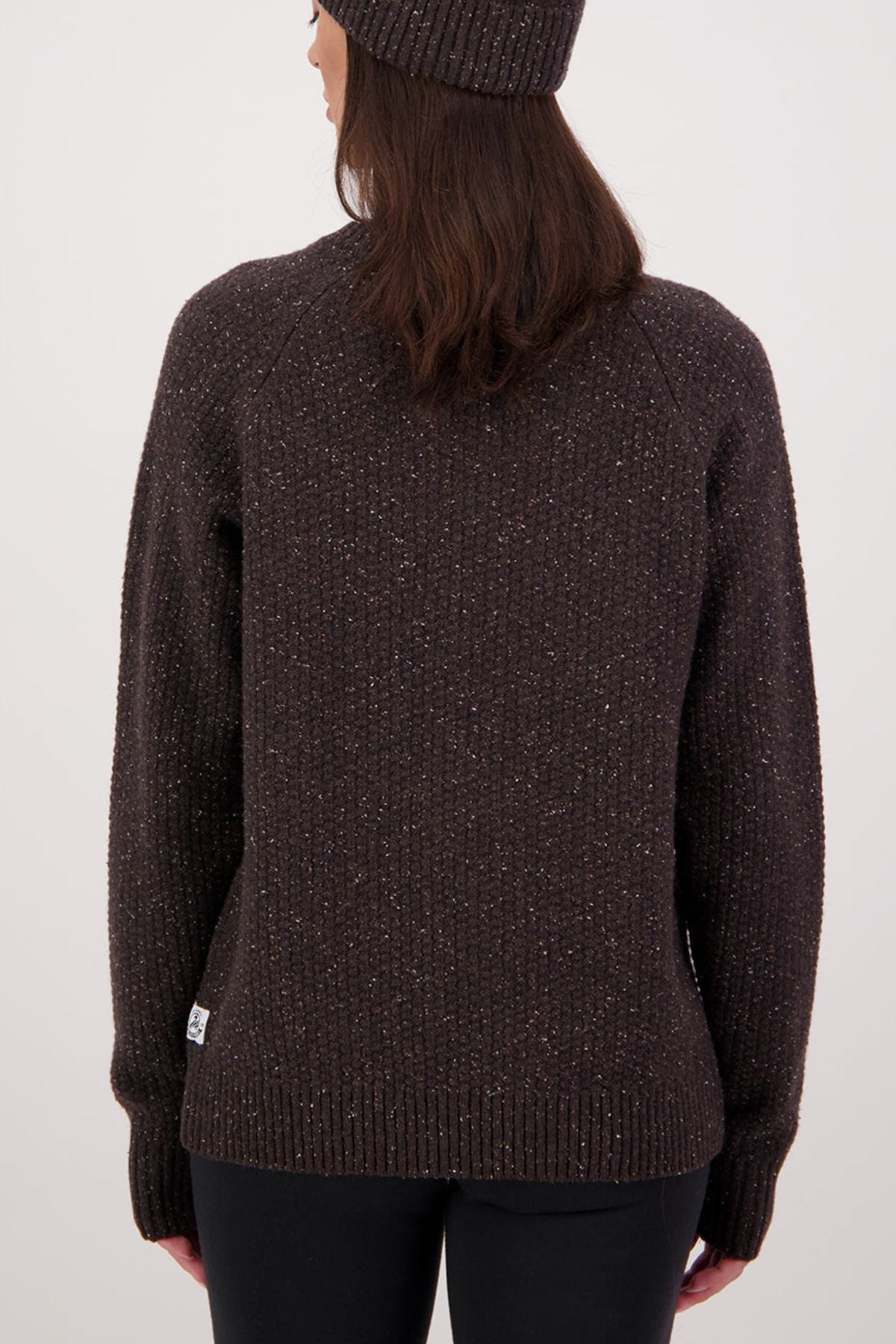 A person with long brown hair wears a brown knit beanie and the Swanndri Lyttelton Womens Waffle Crew, standing with their back to the camera against a plain light background.