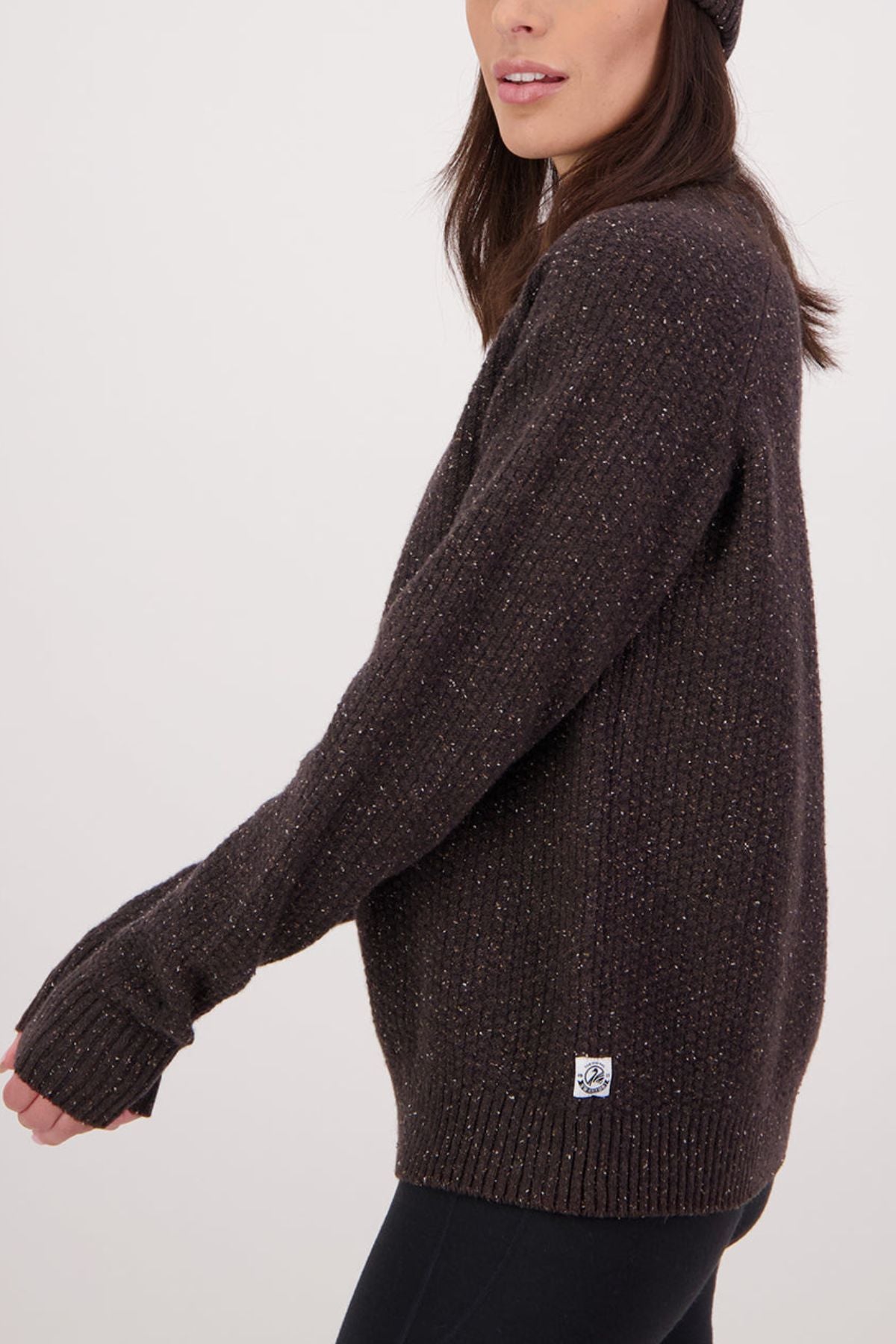 A woman in a dark brown Swanndri Lyttelton Womens Waffle Crew and matching beanie stands sideways against a plain light background, with only her upper body visible as she looks slightly ahead.