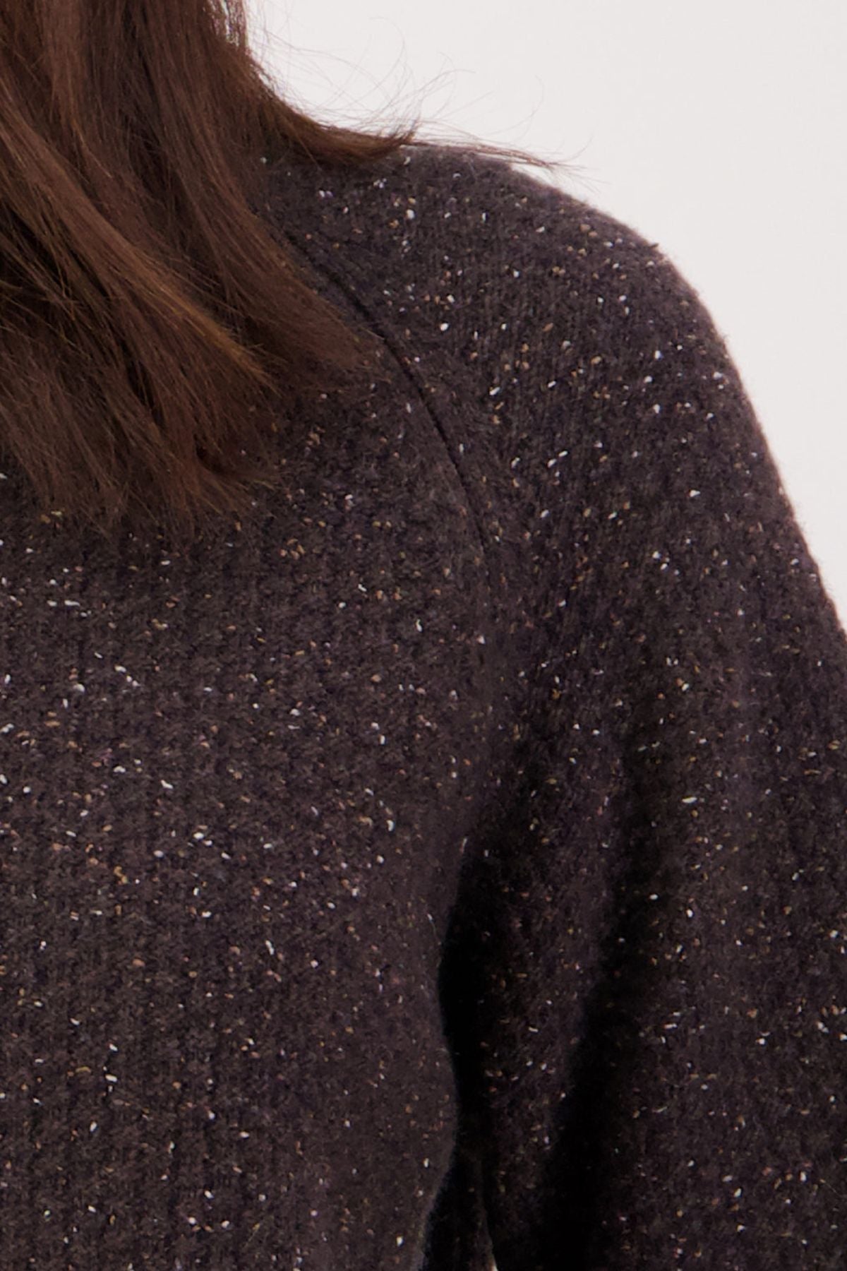 Close-up of a person's shoulder and upper arm wearing the Swanndri Lyttelton Womens Waffle Crew sweater in a dark, textured knit. Only part of their brown hair and neck are visible against a plain, light background.