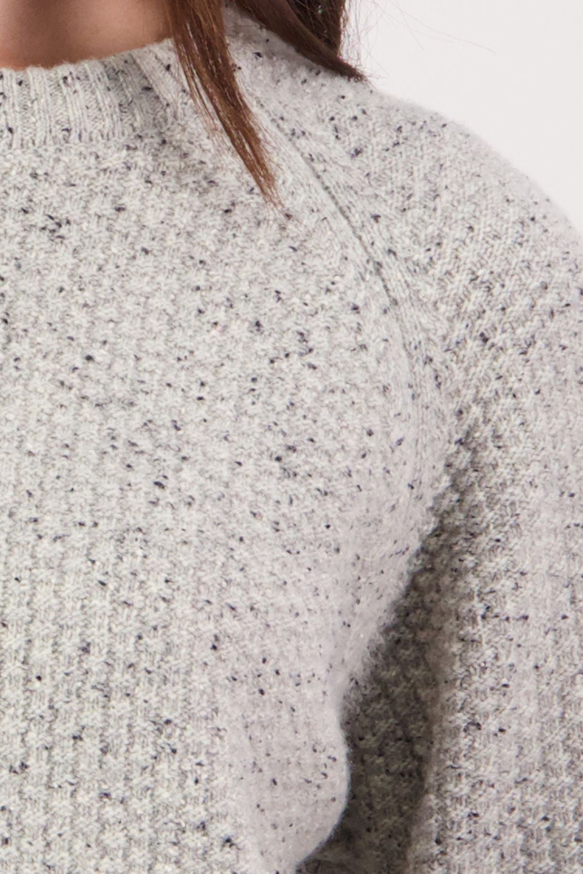 Close-up of a person wearing the Swanndri Lyttelton Womens Waffle Crew, a light gray, textured waffle knit sweater with a speckled pattern. Brown hair partially visible at the top; plain white background.