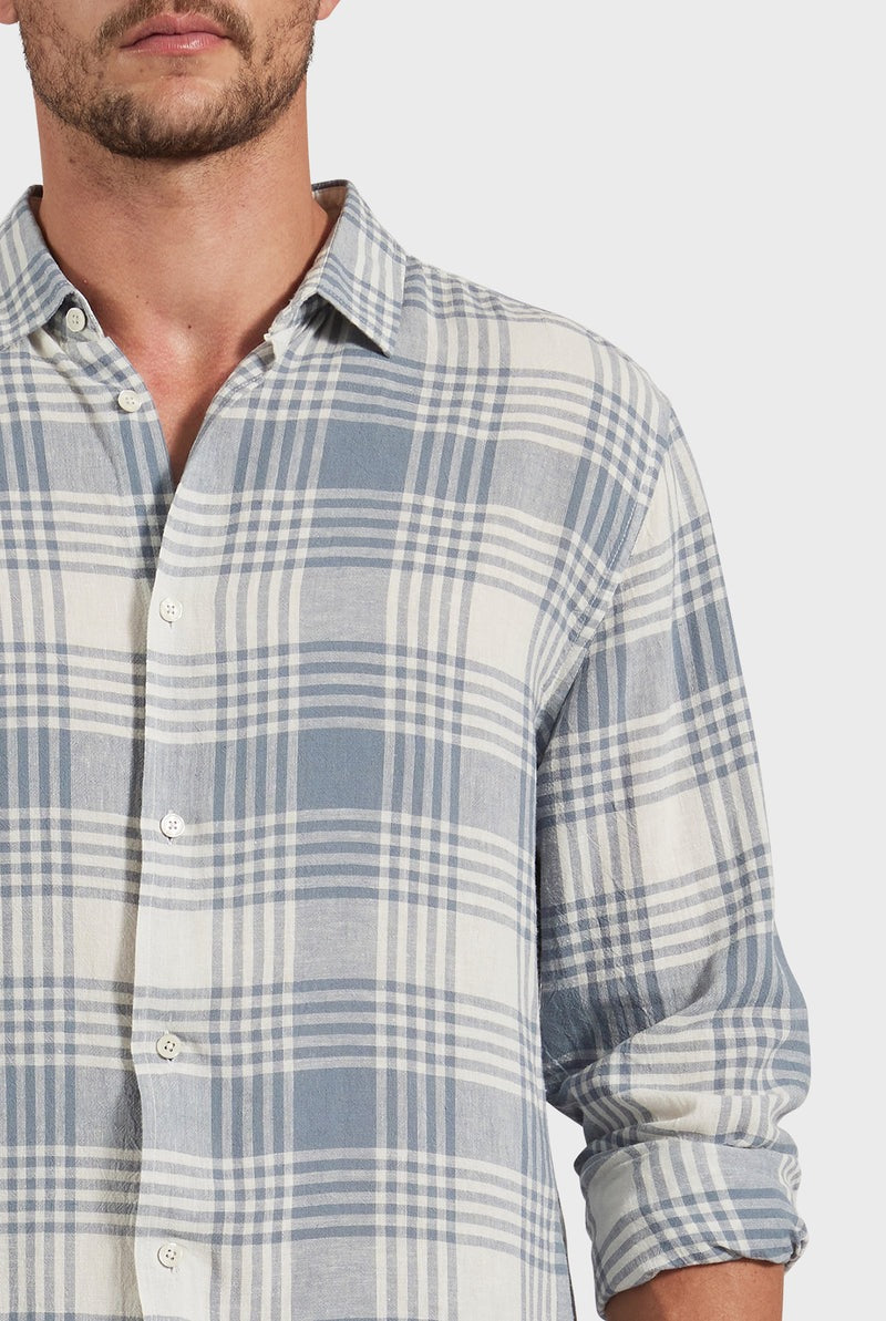 A man is shown wearing the Academy Brand Yosemite Shirt, a blue and white plaid design made from a linen-viscose blend with long sleeves, partially unbuttoned for a relaxed look against a plain white background.