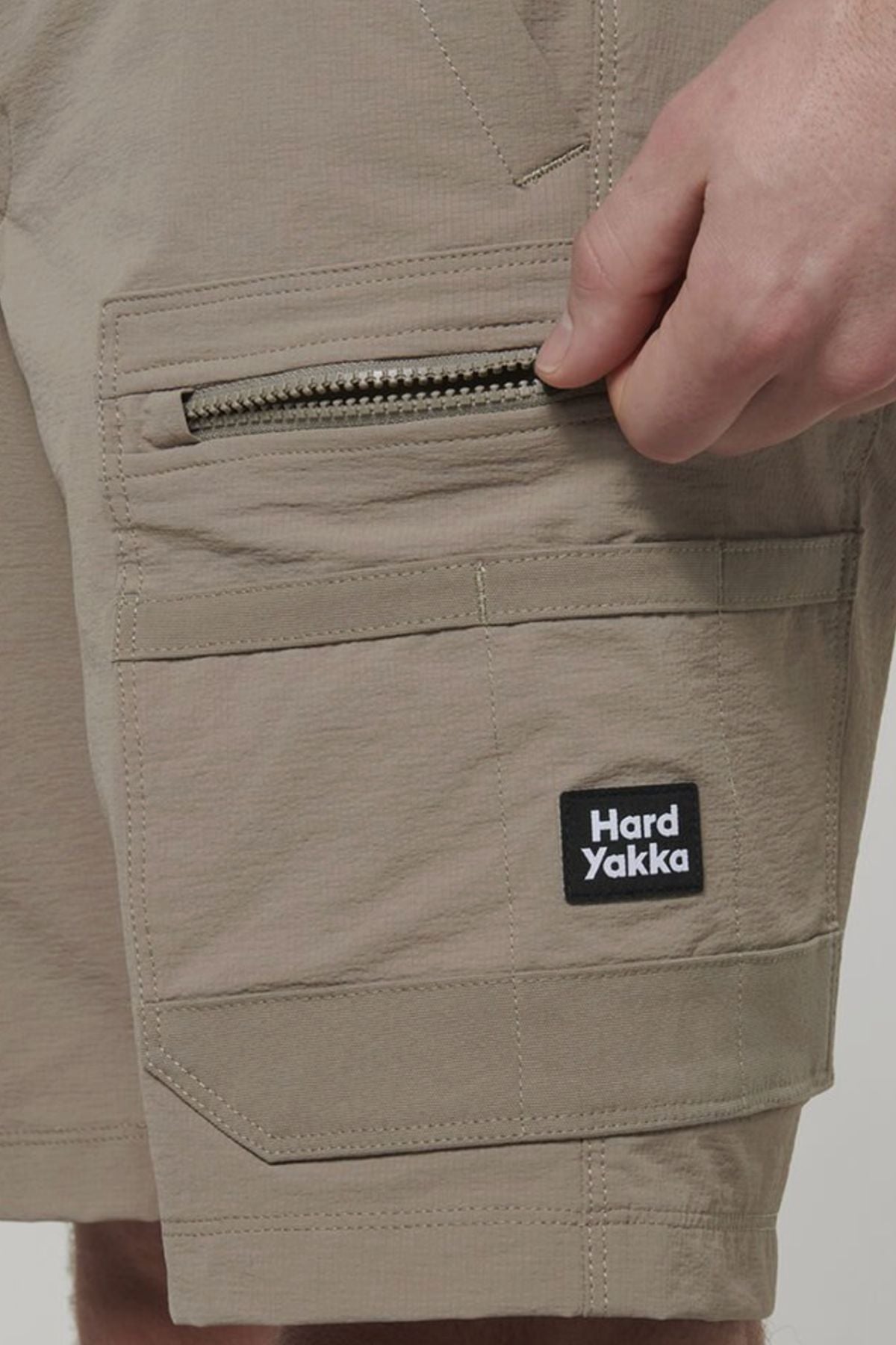 A person's hand holds a zipper in their pocket, highlighting the Hard Yakka X Range Mid Short—durable workwear made from rugged Cordura nylon.
