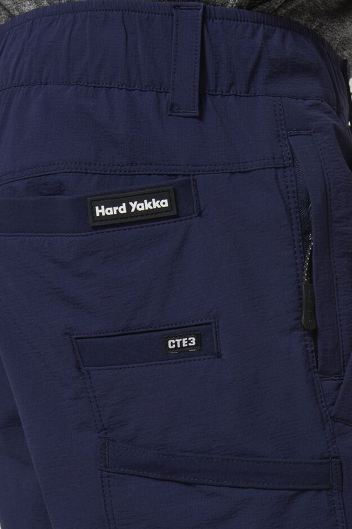 Close-up of a person wearing Hard Yakka X Range Mid Short in navy blue, featuring the brand label, a zippered utility pocket, and a "CTE3" pocket on the upper thigh.