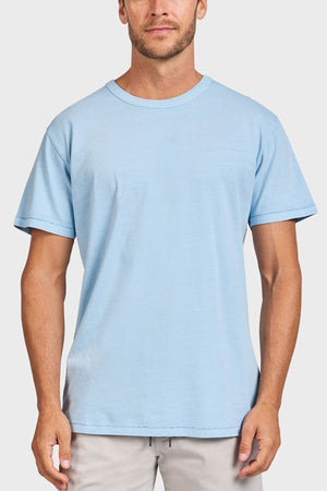 A man faces forward against a white background, wearing the Academy Brand Jimmy Tee in plain light blue and light-colored pants.