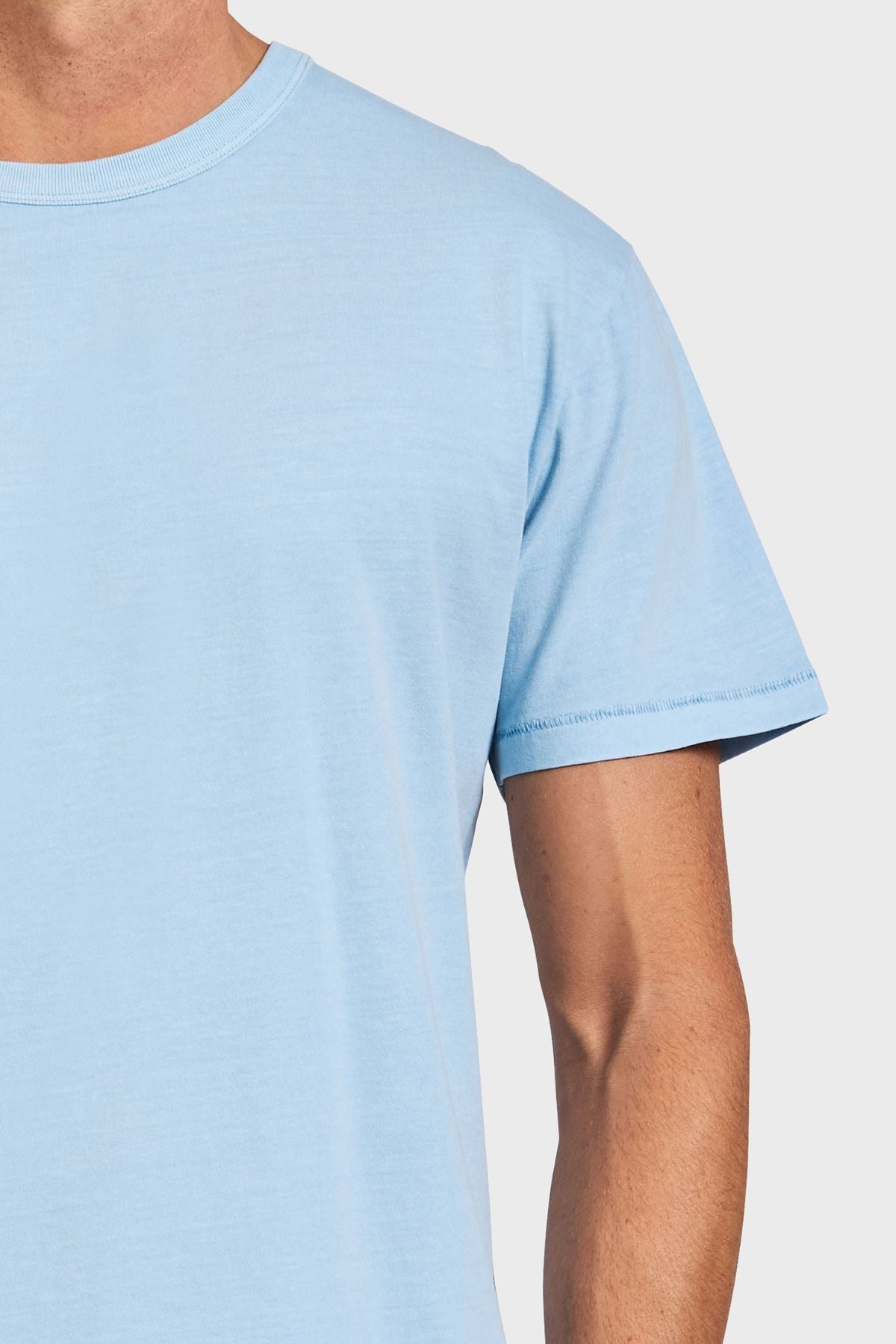 A person wears the Academy Brand Jimmy Tee in light blue, showing only the upper torso and part of one arm against a plain light background.