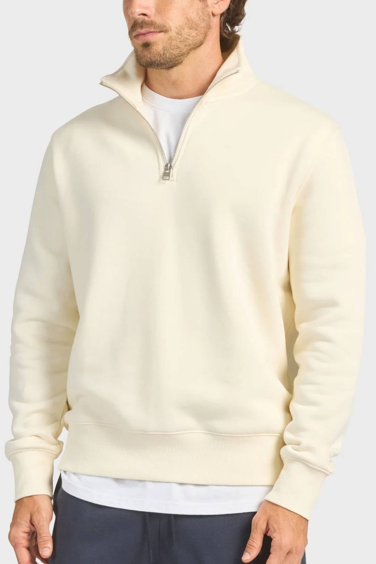 A man wearing the Academy Brand 1/4 Zip Sweat in cream over a white T-shirt and dark pants, shown from the thighs up against a plain light background.