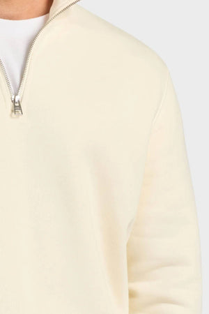 A close-up of someone wearing the Academy Brand 1/4 Zip Sweat in light beige, crafted from premium brushed fleece over a white shirt, highlighting the top zipper and shoulder against a plain light background.