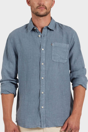 A man in the Academy Brand Hampton Linen Shirt, light blue with a front pocket and rolled-up sleeves, stands against a plain light background.
