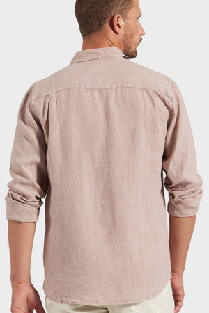 A man stands with his back to the camera, wearing a light pink Academy Brand Hampton Linen Shirt with rolled sleeves and light pants, highlighting the shirt's relaxed comfort and pure linen fabric.
