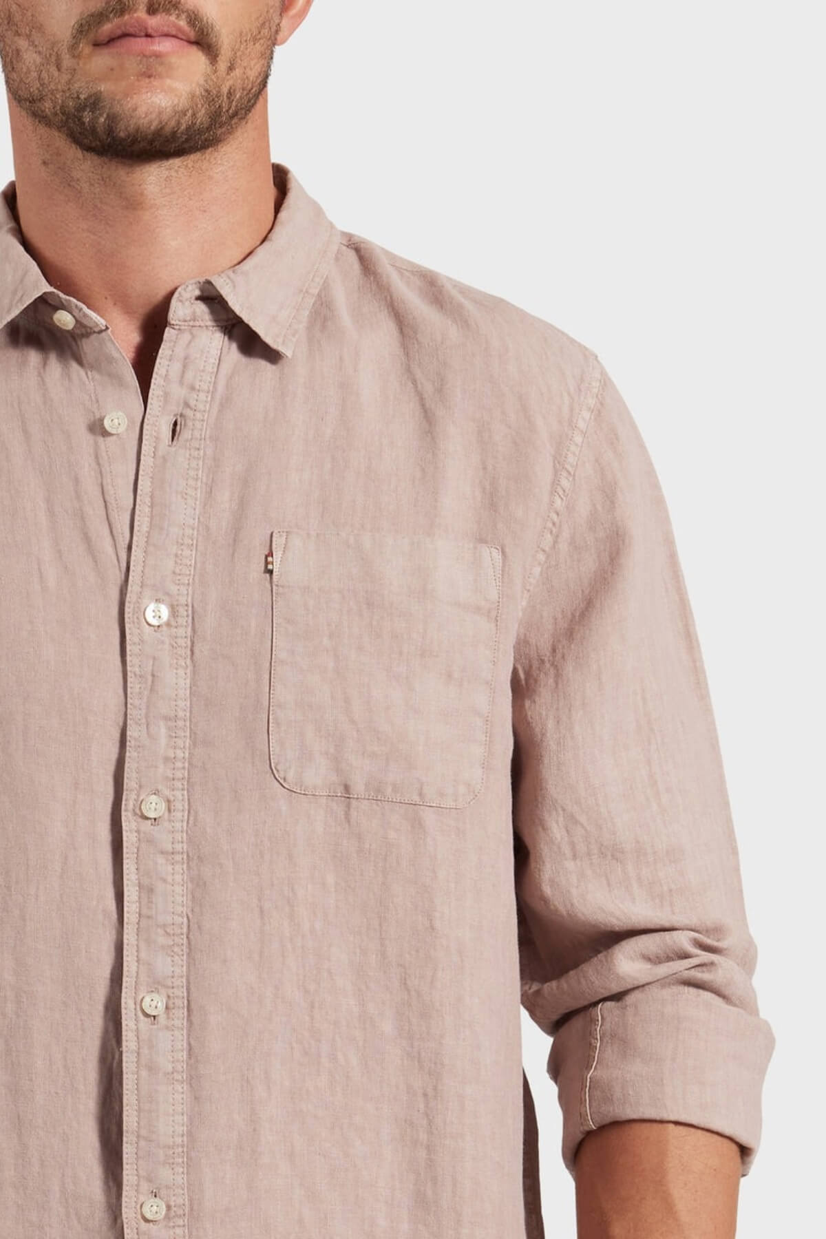 A man wears the Academy Brand Hampton Linen Shirt, a light pink pure linen button-up with a chest pocket and rolled-up sleeves; only the lower half of his face is visible against a plain background.