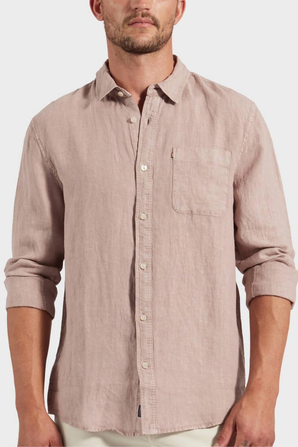 A man wears the Academy Brand Hampton Linen Shirt in light pink linen, featuring rolled-up sleeves and a front pocket, standing facing forward against a plain background.