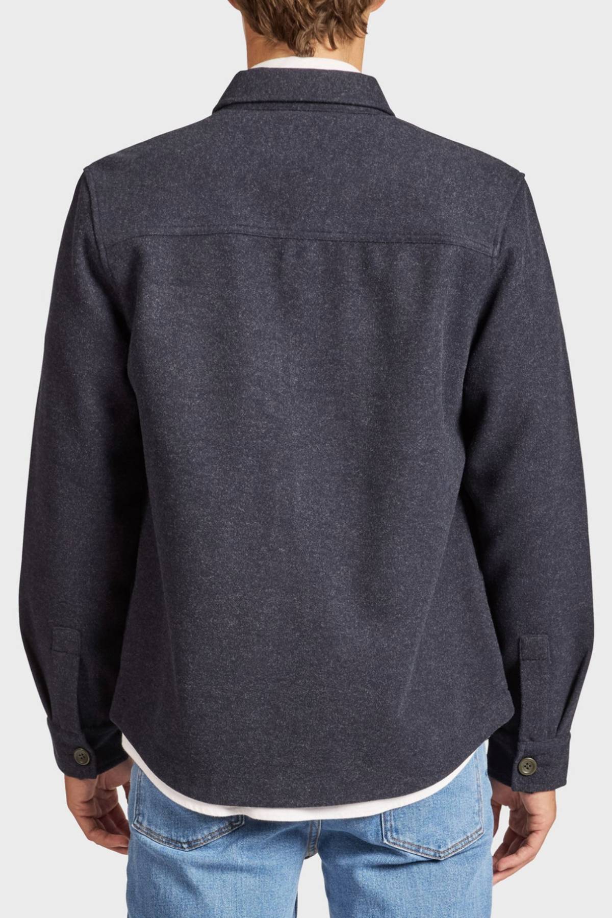 A man is seen from behind wearing the Academy Brand Lloyd Overshirt in dark gray, layered over a white shirt and light blue jeans. The photo focuses on the back and sleeve features of the overshirt.