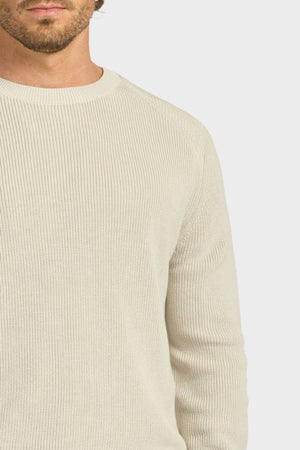 Cropped image of a man wearing the Academy Brand Oliver Knit Crew—a light beige, ribbed cotton sweater with long sleeves—shown from shoulders to waist against a neutral background.