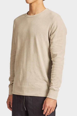 A person wearing the Academy Brand Workers Crew long-sleeve shirt in beige with dark pants, shown from shoulders to hips, stands against a plain light background.