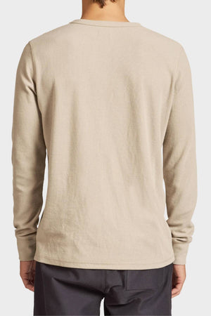 A person is shown from the back wearing the Academy Brand Workers Crew, a durable light beige long-sleeve shirt with dark pants. Its plain French rib design offers a clean, classic look with no visible logos or patterns.