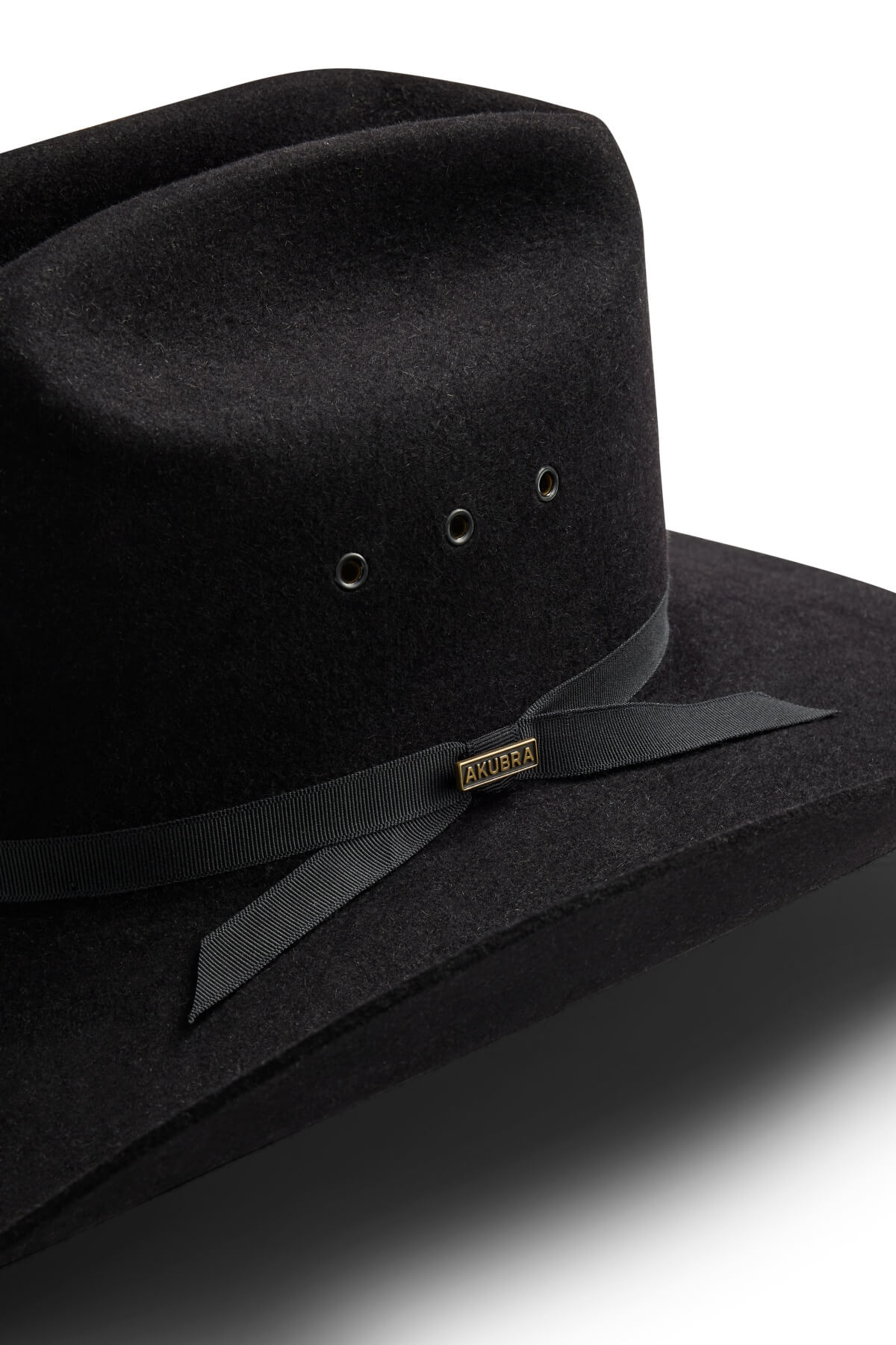 Close-up of the Akubra Outback Club hat, a black wide-brimmed style with a black ribbon and bow, metal ventilation eyelets, a small rectangular "Akubra" label, reflecting the iconic look of Australian country music.