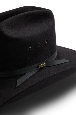 Close-up of the Akubra Outback Club hat, a black wide-brimmed style with a black ribbon and bow, metal ventilation eyelets, a small rectangular "Akubra" label, reflecting the iconic look of Australian country music.