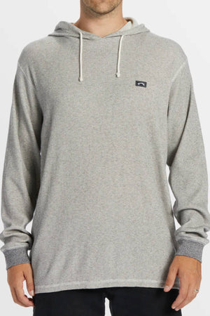 A person wearing the Billabong Keystone Pullover, a light gray long-sleeve hoodie with white drawstrings and a small rectangular logo on the left chest, stands against a plain background.