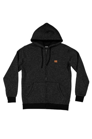 The Billabong Revolt Zip Thru Hood is a dark gray hoodie in cotton-blend textured fleece, with black cuffs, waistband, and drawstrings. It features front pockets and a small brown rectangular patch on the left chest.