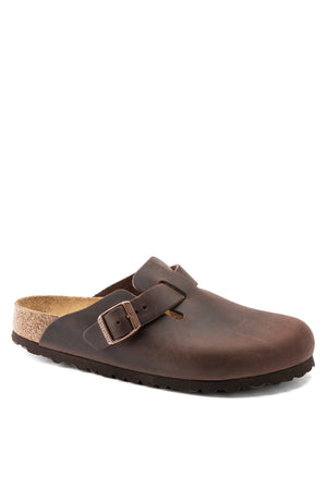 The Birkenstock Boston is a brown leather slip-on clog with an adjustable strap, anatomically shaped cork footbed, and a dark brown rubber sole, shown on a white background.