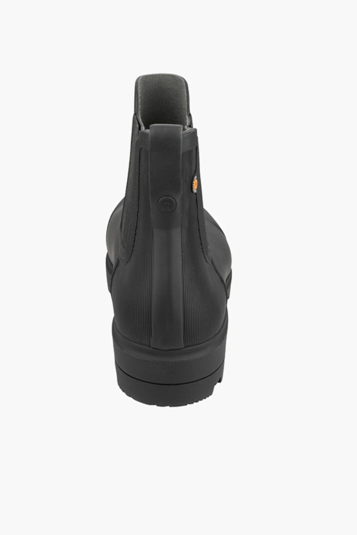 The BOGS Holly Chelsea Waterproof Boots in black are ankle-high, shown from the back with a pull tab, subtle heel ridges, and BLOOM Algae Footbeds for comfort, all set against a plain white background.