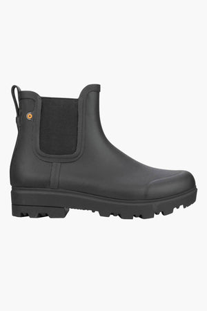 The BOGS Holly Chelsea Waterproof Boots are black slip-on rubber Chelsea boots with a rugged sole, elastic side panels, waterproof design, and BLOOM Algae Footbeds for comfort; displayed in a side profile on a white background.