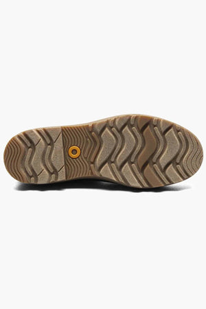 The image shows the sole of the BOGS Holly Chelsea Waterproof Boots, featuring a textured, wavy tread and a circular yellow detail on a light brown rubber surface with BLOOM Algae Footbeds for enhanced comfort.
