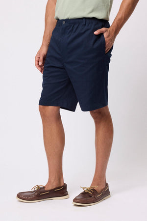 A person stands against a plain white background with hands in pockets, wearing a light green T-shirt, Breakaway Cody Shorts with an elastic waistband, and brown boat shoesβideal for effortless everyday style.