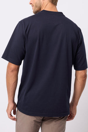 A man stands facing away from the camera wearing a relaxed fit Breakaway Kinnersly Crew in dark navy with light brown pants, set against a plain light background.