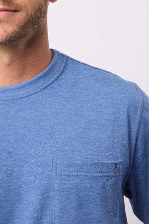 A close-up shows a man in the Breakaway Kinnersly Crew, a relaxed-fit blue tee with a chest pocket. The image features only his lower face, neck, and upper torso set against a plain light background.
