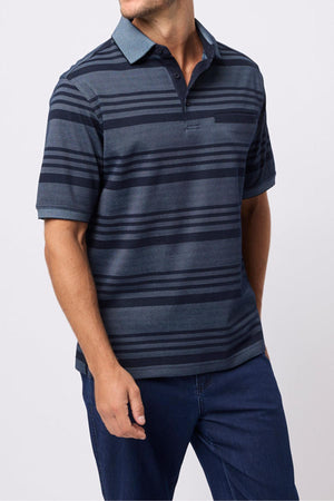 A man wearing a navy Breakaway Ryle Micro Prima Polo and blue jeans stands with one hand by his side and the other partially visible, against a plain light background.