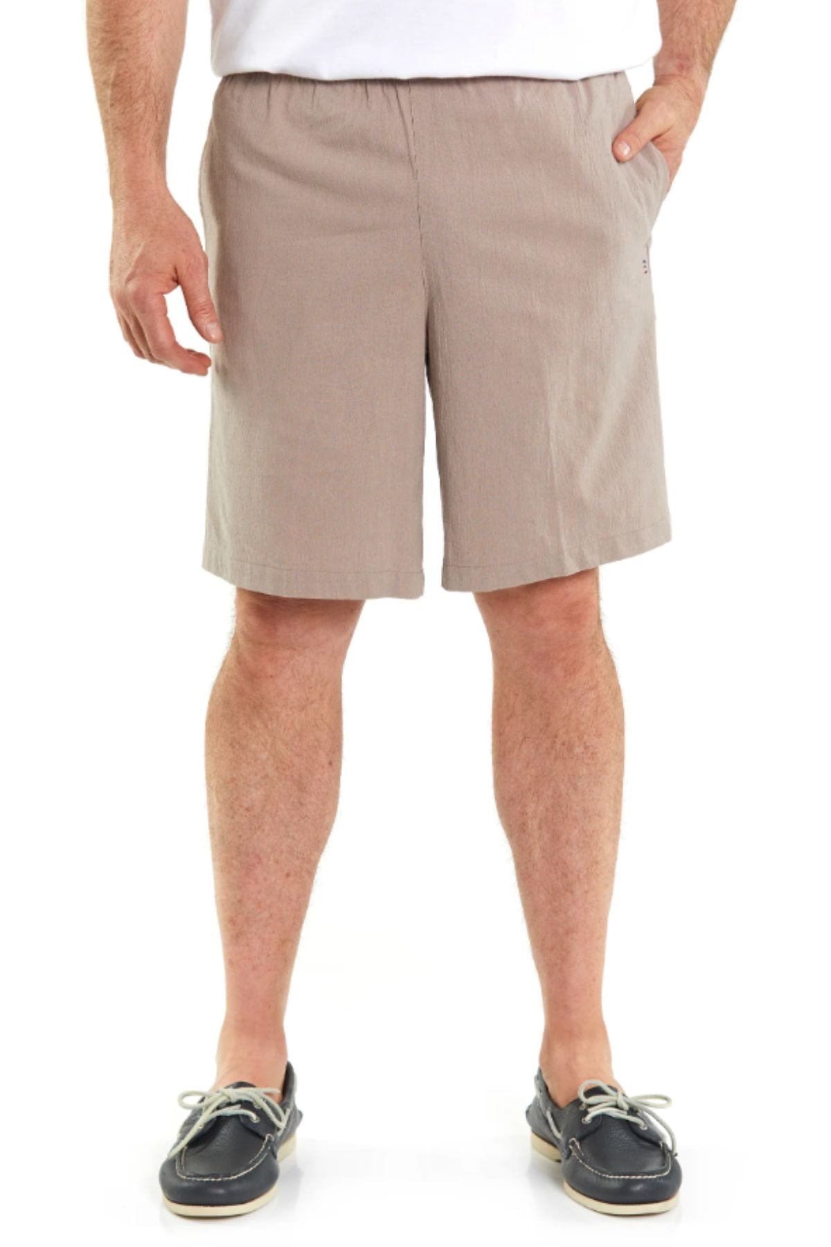 A man wearing light brown Breakaway Woodbury Shorts with an adjustable waist, a white shirt, and black boat shoes with white laces stands with one hand in his pocket against a plain white background.