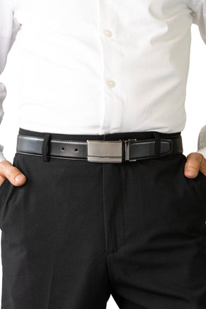 A person wears a white dress shirt tucked into black dress pants with the Buckle 5519 Heritage 35mm Reversible Leather Belt, featuring a silver rectangular buckle, and stands with hands in their pockets.