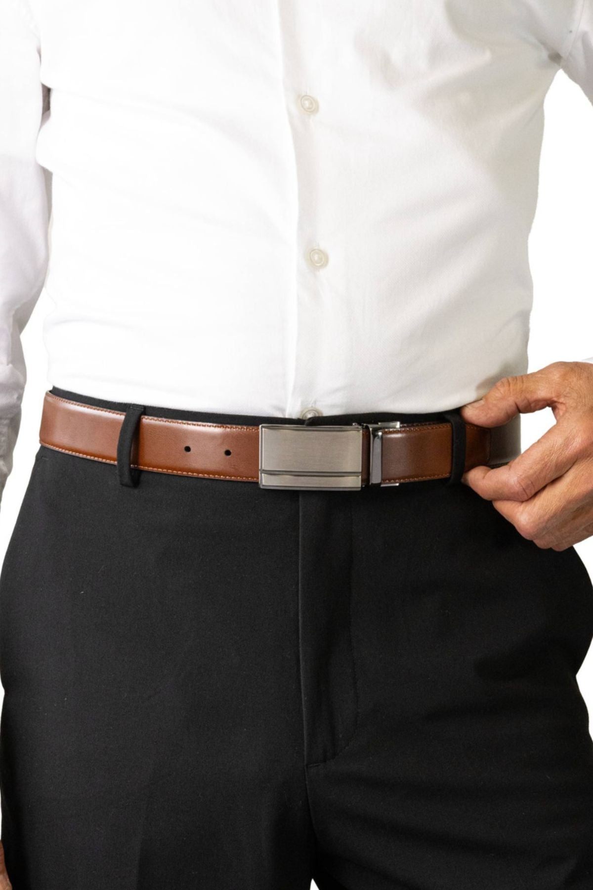 A person adjusts the Buckle 5519 Heritage 35mm Reversible Leather Belt, styled with a white dress shirt tucked into black pants.