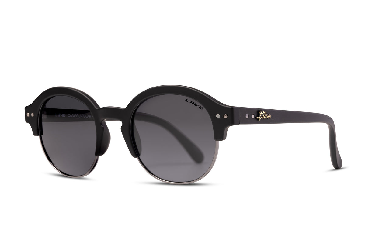 The Liive Canggu Polar Sunglasses are a pair of black round sunglasses with dark lenses that offer UV protection. The frame features a retro design and has small silver accents near the hinges. The temples display a gold logo, and the inner side of the right temple displays the text "LINE VANGOGH.