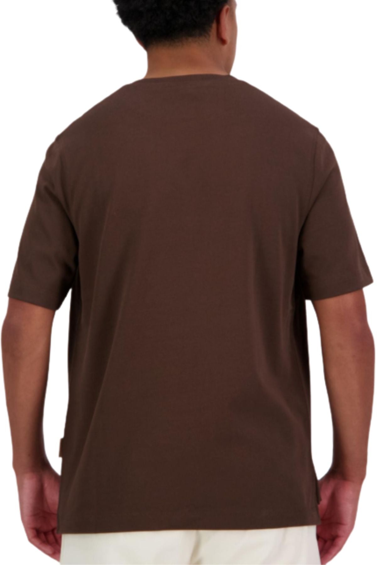 A person with short curly hair is seen from behind wearing an oversized brown Canterbury CCC Collection T-Shirt and light-colored pants against a white background.