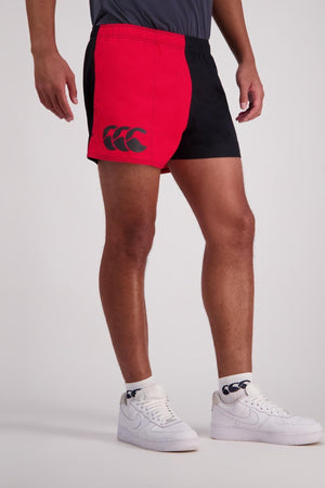 A person sporting a pair of black and red Canterbury Cotton Twill Harlequin Shorts, featuring breathable cotton and adorned with a logo on the side. The look is complemented by a gray shirt, white socks, and white sneakers.