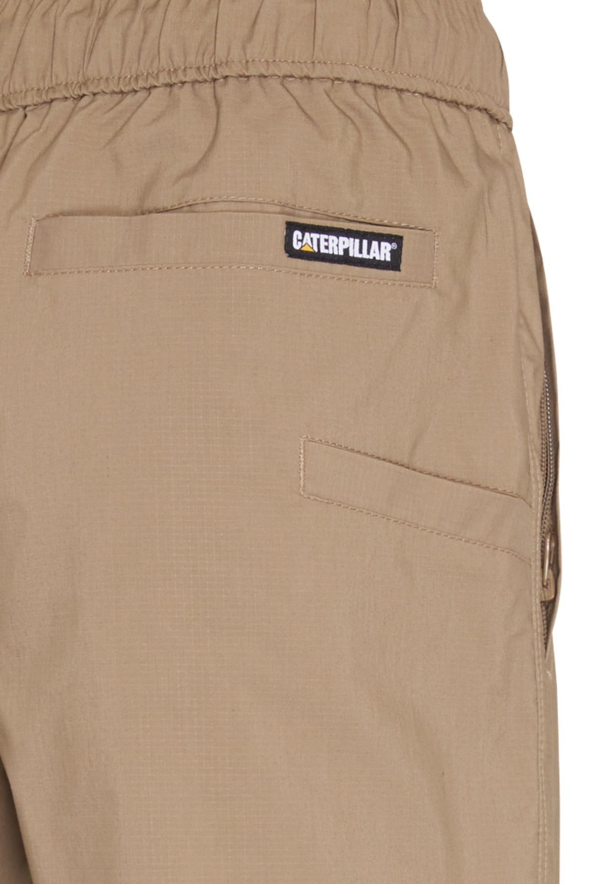 Close-up of the back pocket area on CAT Hydraulic Short, tan stretch work shorts with an elastic waistband, Caterpillar label above the pocket, and visible stitching.