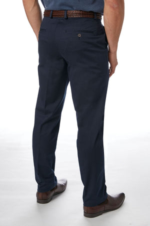 A person is standing with their back to the camera, showcasing the stylish and comfortable City Club Navigator 1770 Pants. They are wearing dark blue, slim-fit trousers paired with a woven brown belt and brown shoes. Made from Cotton and Spandex, these trousers fit perfectly. The plain white background ensures that the person remains the main focus of the image.
