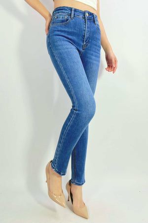 A person models the Country Denim Ankle Length Stretchy Jean in blue with beige pointed-toe heels, standing against a white background, arms relaxed and one leg slightly bent.