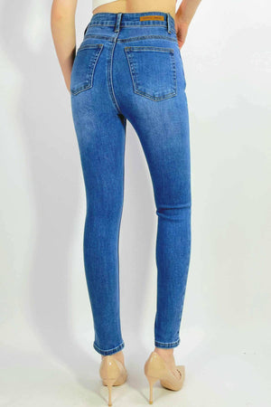 A person stands against a white background, facing away with hands on hips, wearing Country Denim Ankle Length Stretchy Jeans in blue and nude high-heeled shoes.