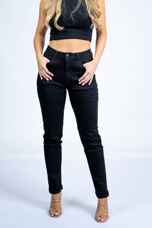 A woman stands against a plain white background wearing a black sleeveless crop top, Country Denim Relaxed Mum Jean high-waisted black jeans, and nude strappy heels. Her hands are in her pockets, with her head out of frame.
