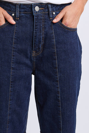 A person wearing Foxwood Ambrose Barrel Jeans in dark blue, featuring a high-waisted barrel fit, visible front seams, contrast stitching, and hands in the front pockets.