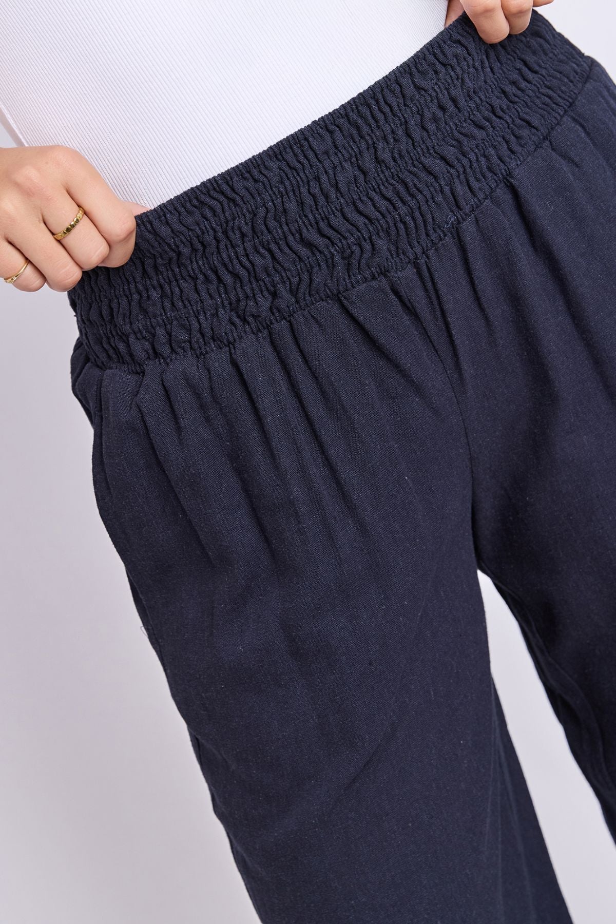 A person is shown from the waist down wearing the Foxwood Amie Pant in navy blue, styled with a white top and one hand resting on the waistband.