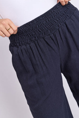 A person is shown from the waist down wearing the Foxwood Amie Pant in navy blue, styled with a white top and one hand resting on the waistband.